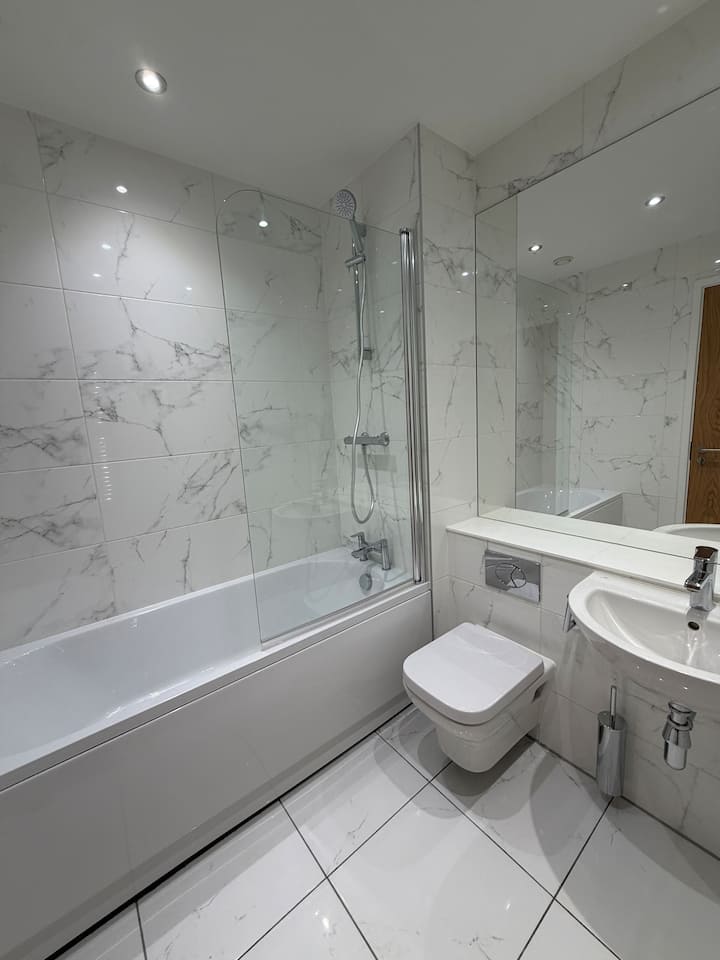 White tiled bathroom with a bath and glass shower screen